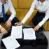 Colleagues reviewing employment agreements at a glass table, seated on a yellow sofa, business attire, close-up shot